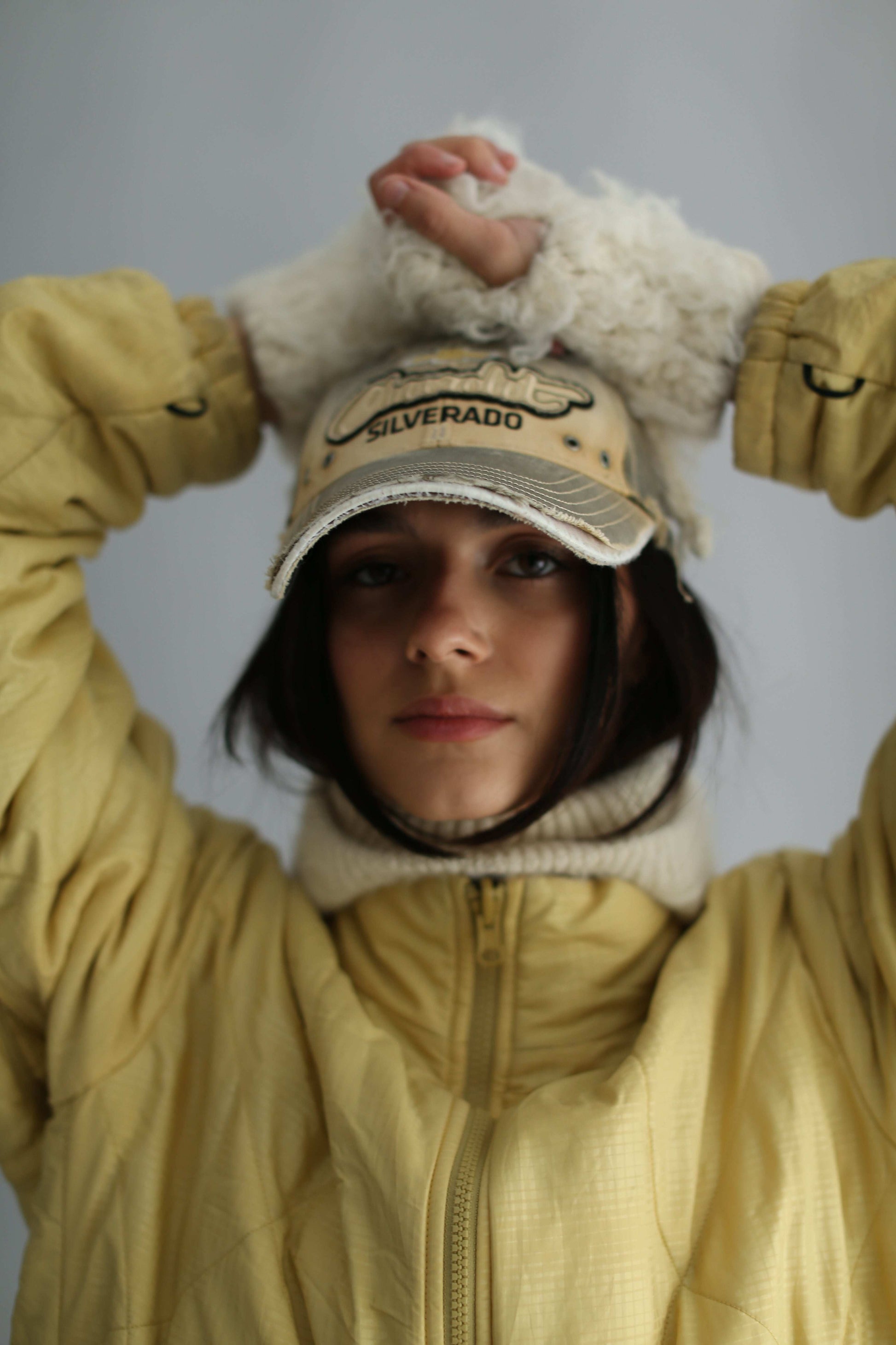 Portrait of a model wearing a white balaclava, a cap and a yellow jacket against a white background