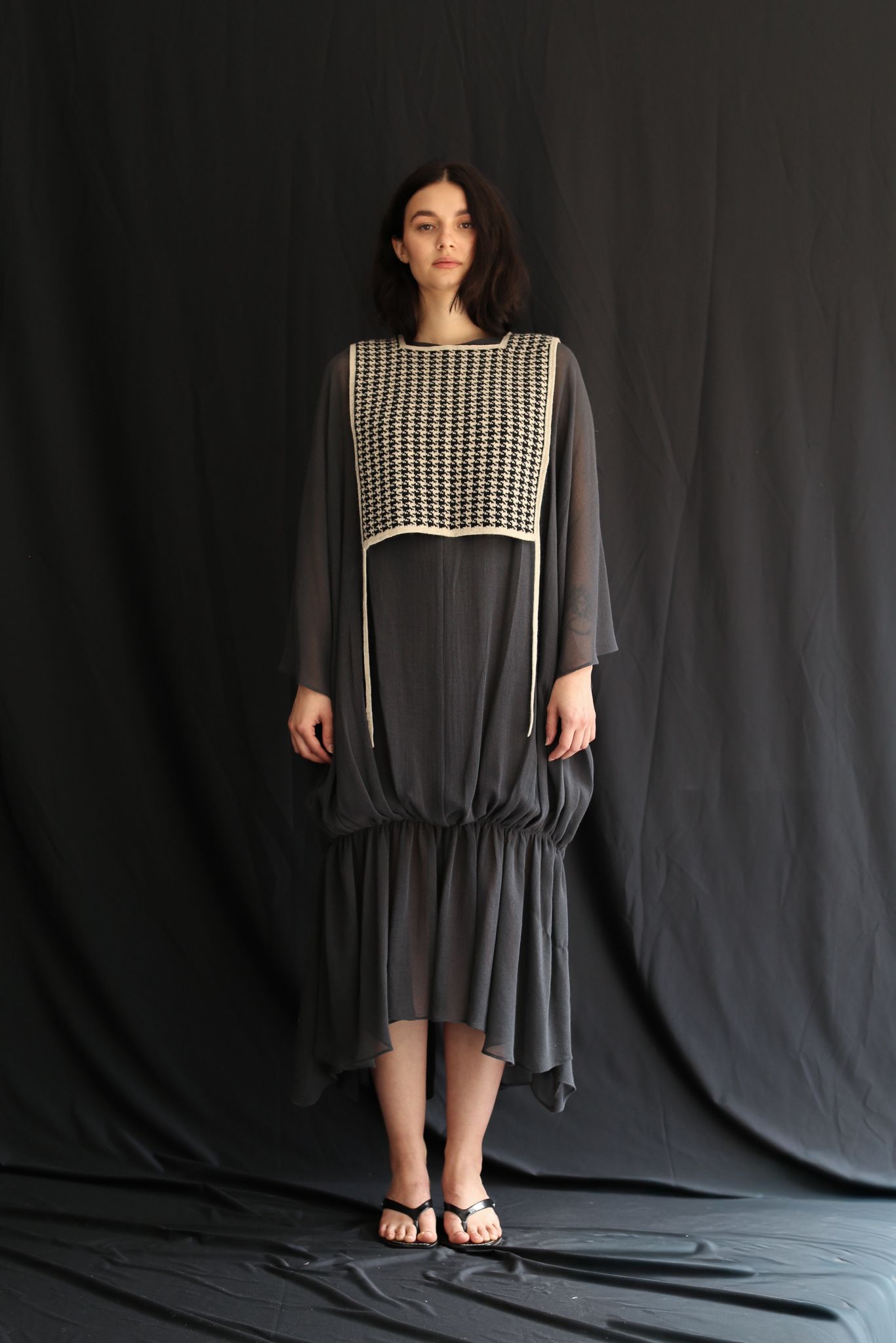 Woman wearing a dark gray dress with a houndstooth patterned top against a black background