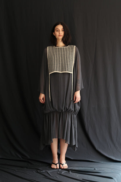 Woman wearing a dark gray dress with a houndstooth patterned top against a black background