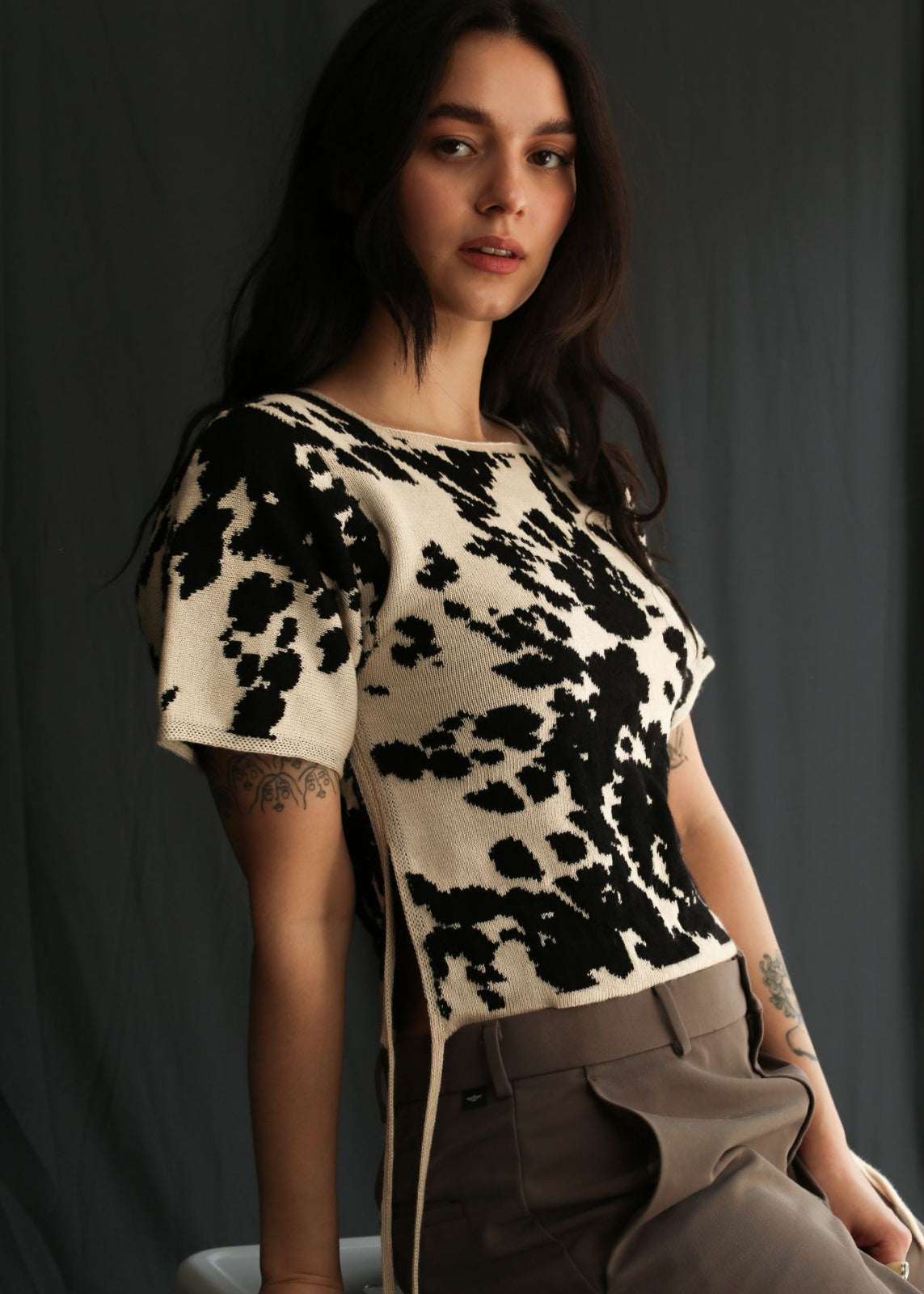 Woman wearing a cow patterned knitted t-shirt top against a black background, half sit