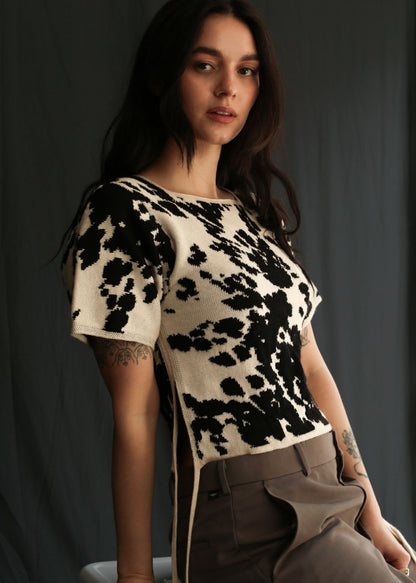 Woman wearing a cow patterned knitted t-shirt top against a black background, half sit
