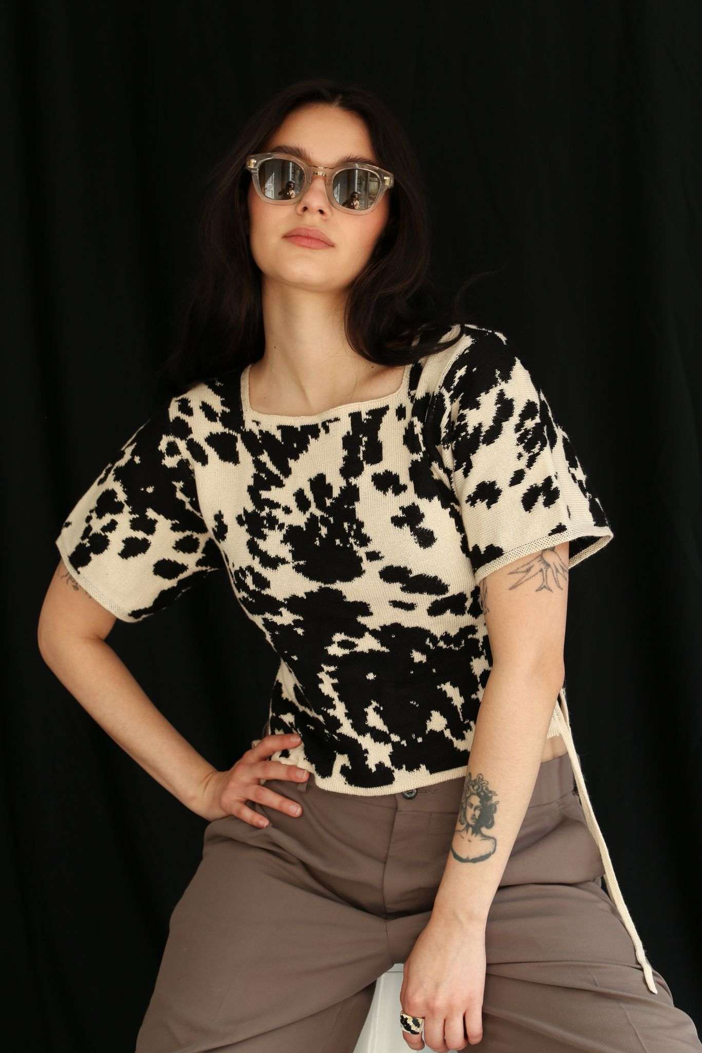 Woman wearing a cow patterned knitted t-shirt top against a black background, half sit