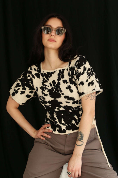 Woman wearing a cow patterned knitted t-shirt top against a black background, half sit