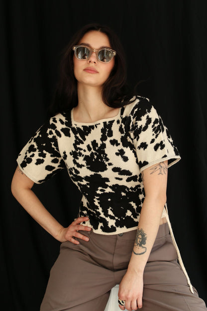 Woman wearing a cow patterned knitted t-shirt top against a black background, half sit