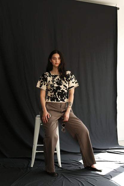 Woman wearing a cow patterned knitted t-shirt top against a black background, half sit